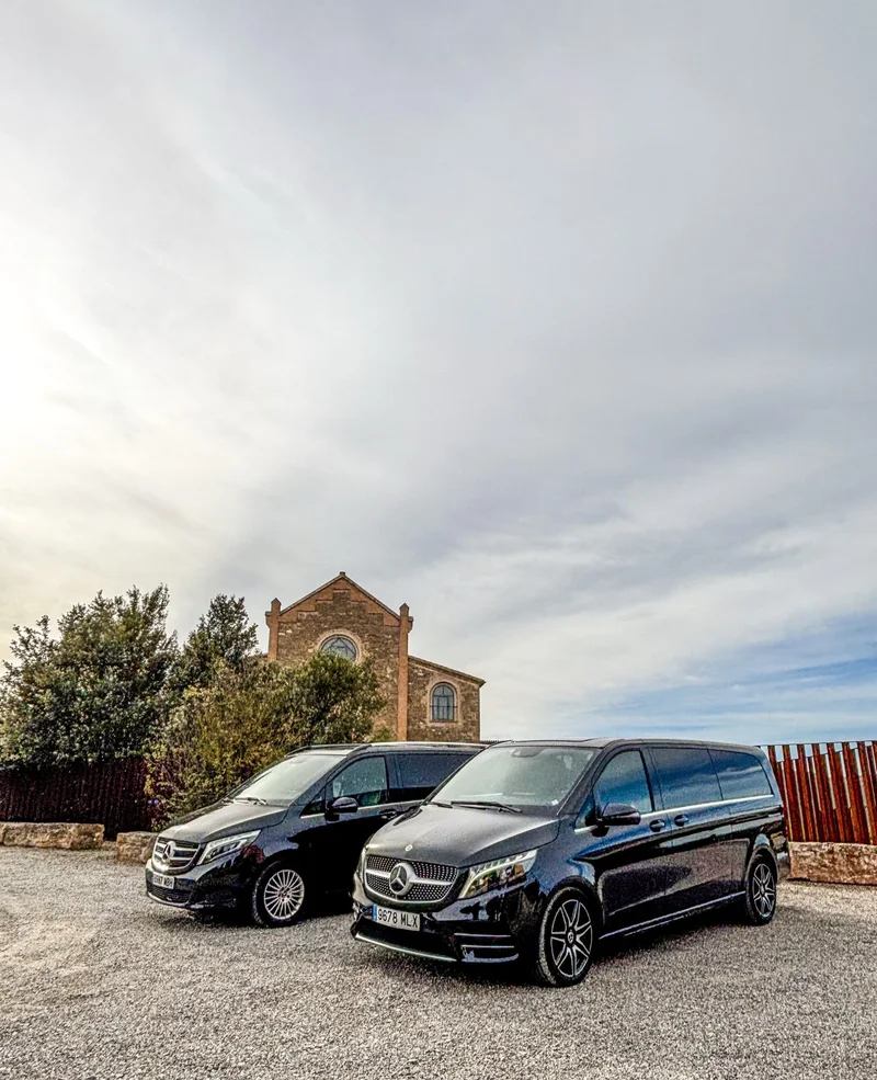 Dos monovolúmenes Mercedes-Benz negros de Black Button aparcados frente al edificio de piedra de Rectoria Godmar