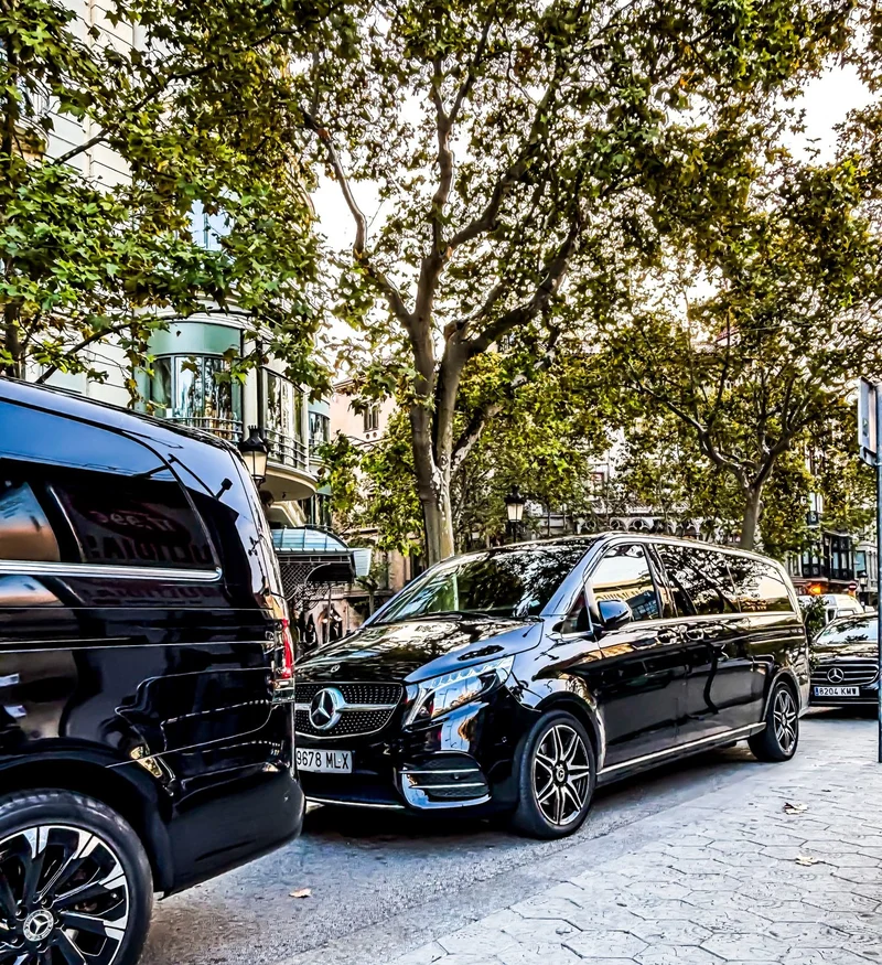Vehículos negros Mercedes-Benz de Black Button Chauffeur Service estacionados en una calle arbolada de Barcelona